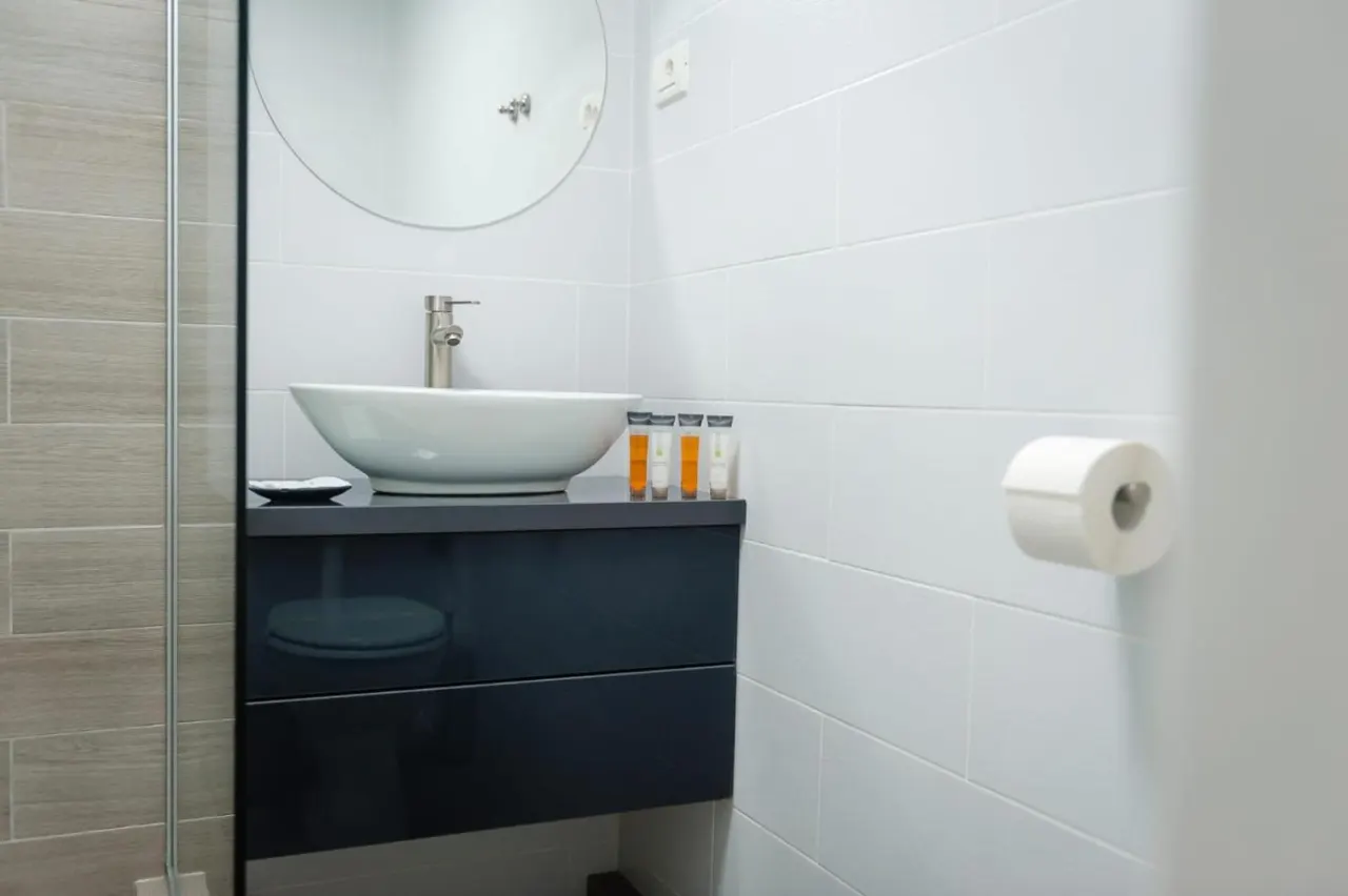 Baie cu chiuvetă tip bol pe blat negru și oglindă rotundă