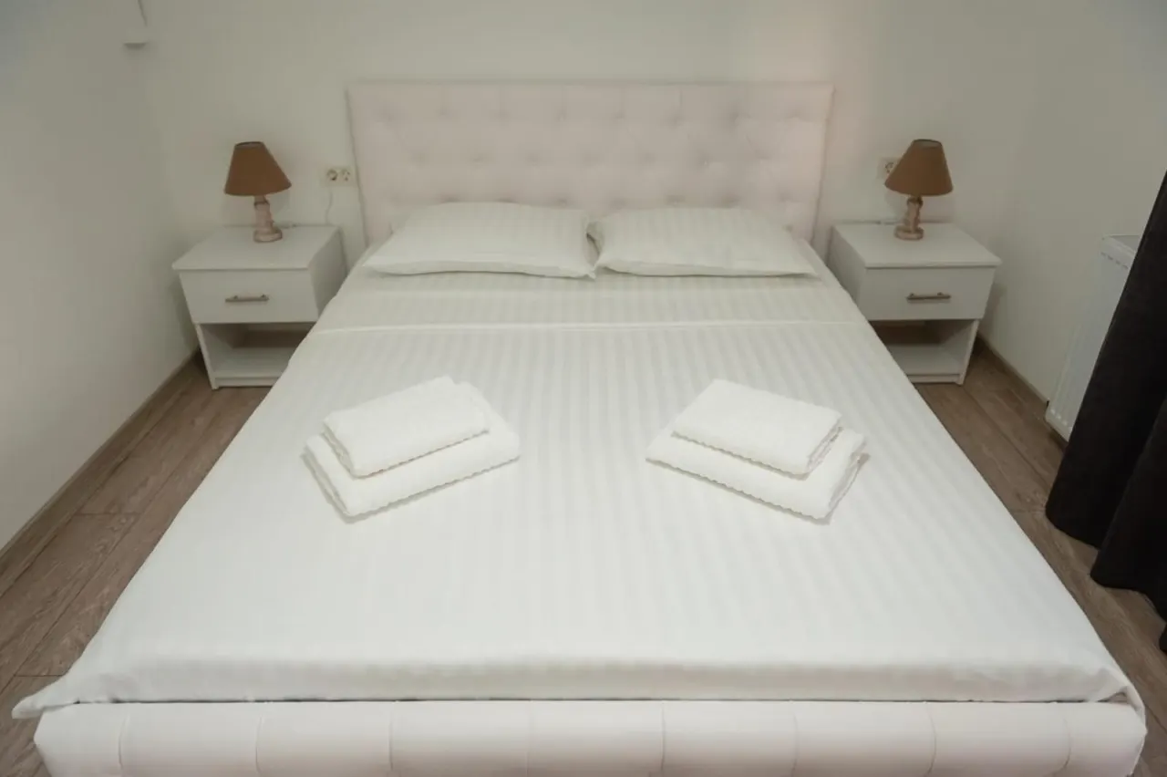 Pat matrimonial cu lenjerie albă și două noptiere cu veioze