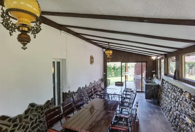 Terasa acoperită, cu mese lungi de lemn, perete de piatră și grinzi